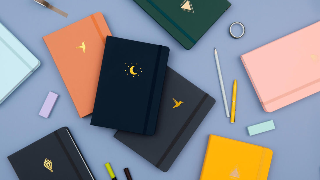 Range of dot grid journals in blue, pink and charcoal with moon and star emblem on white background