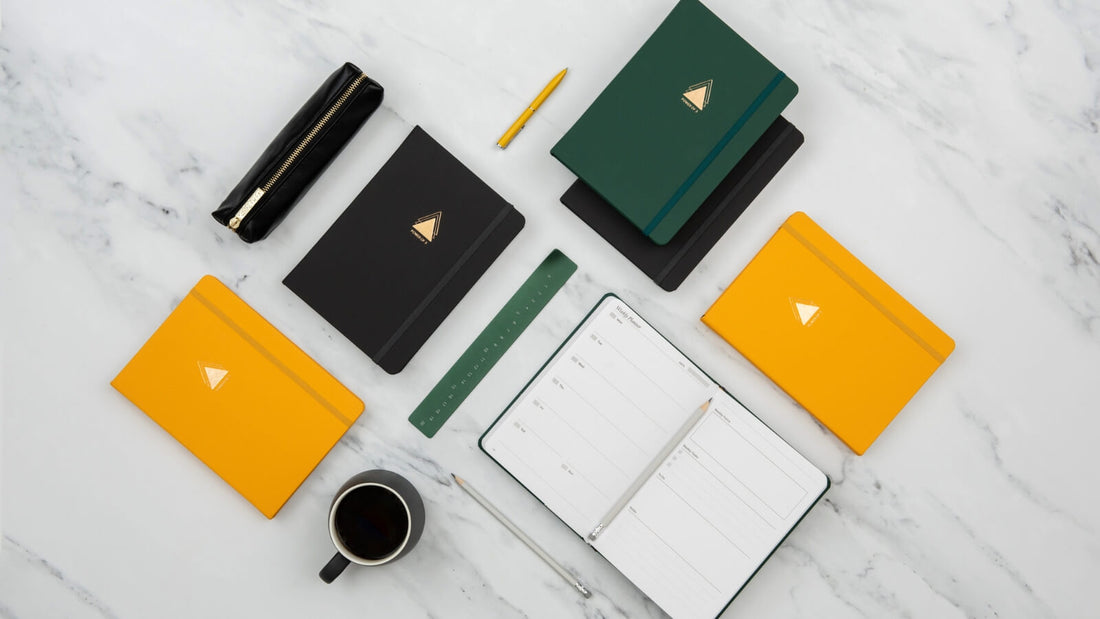 Collection of undated goal planners with triangle emblem in forest green, charcoal and sunshine yellow